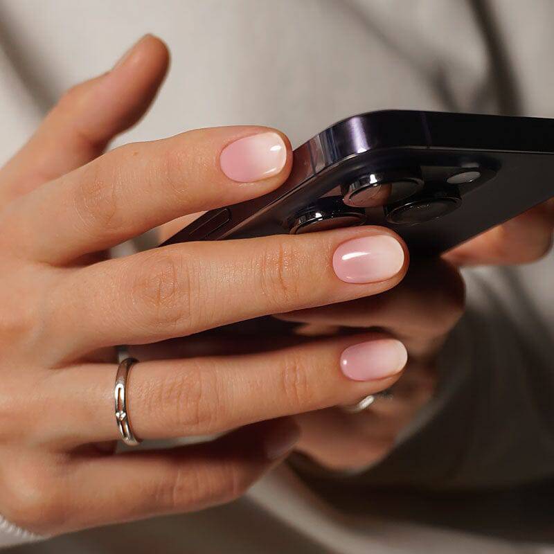 Subtle ombre manicure in pink and white tones, paired with a sleek black smartphone.