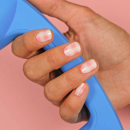  Close-up of nails featuring pink and white checkered patterns. The hand is holding a blue item against a pastel pink background.