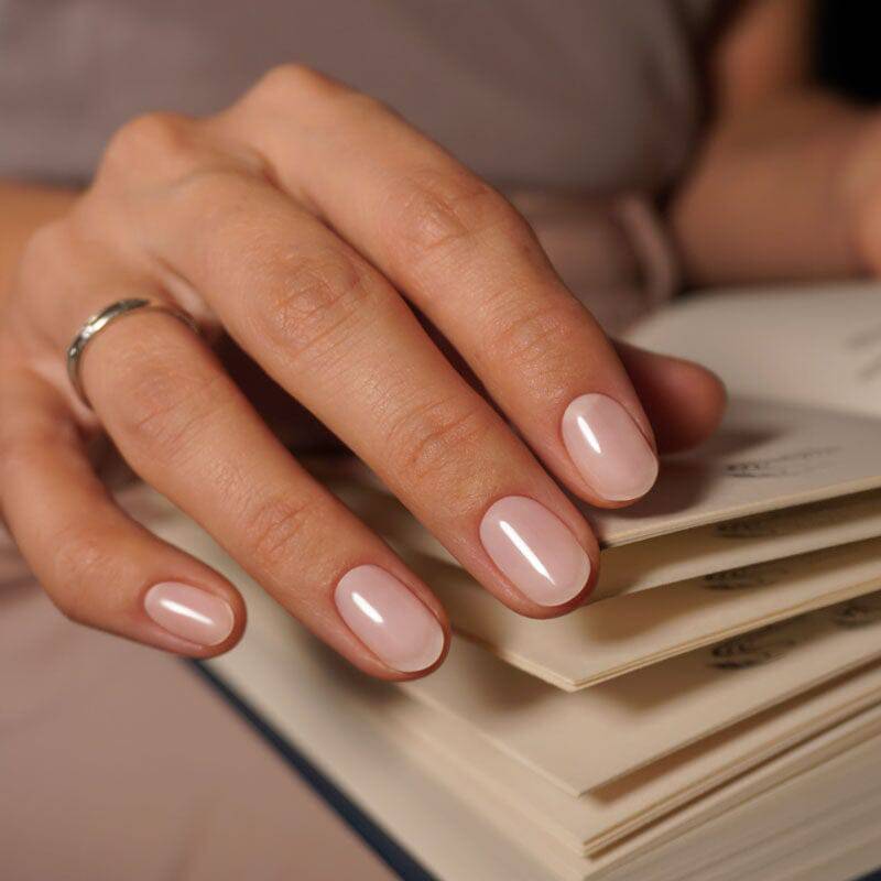 Minimalist pink nails with a glossy sheen, styled against a cream-toned backdrop.