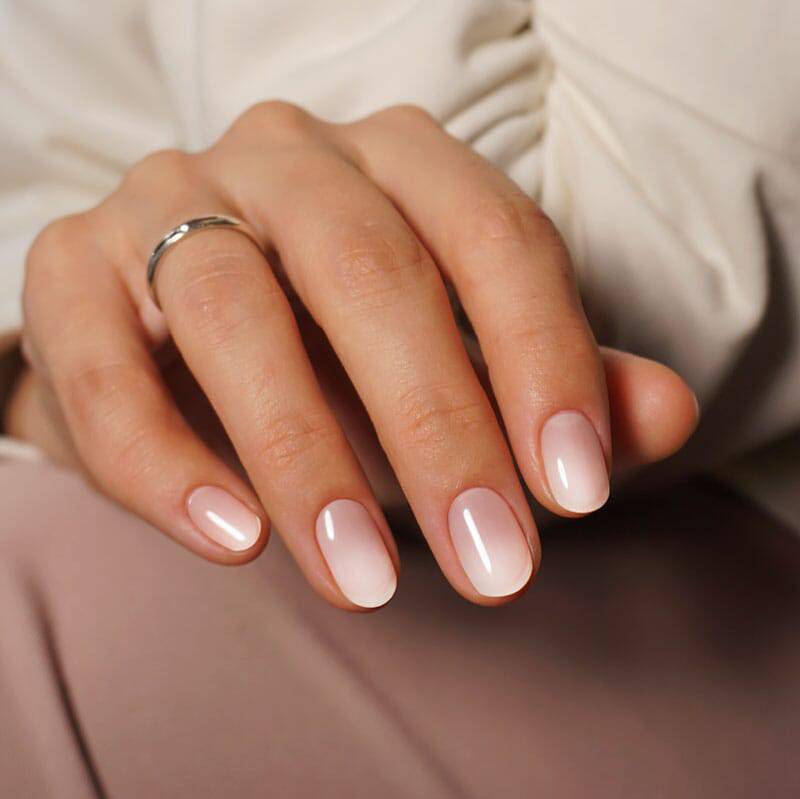  A close-up of ombre nails transitioning from light pink to white. The hand is holding a smartphone, adding a contemporary element.