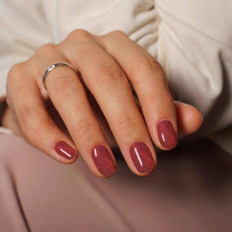 Berry red nails with a shimmering cat eye finish, styled for an elegant and polished appearance.
